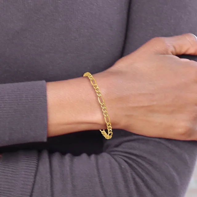 A person wearing a gray long-sleeved garment displays a gold-toned curb chain bracelet on their wrist.