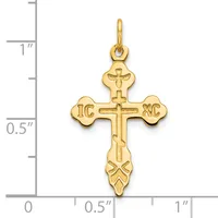 Gold-toned cross pendant with ornate ends featuring "IC XC" initials and decorative flourishes, shown against a measurement scale.