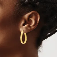 A person wearing a pair of polished gold-colored hoop earrings with a rounded, tubular design.