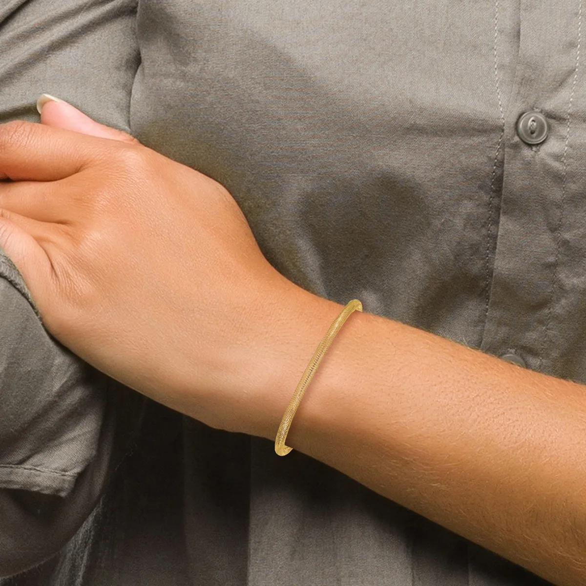 A person wearing a gray button-up shirt displays a gold-toned bangle bracelet on their wrist.