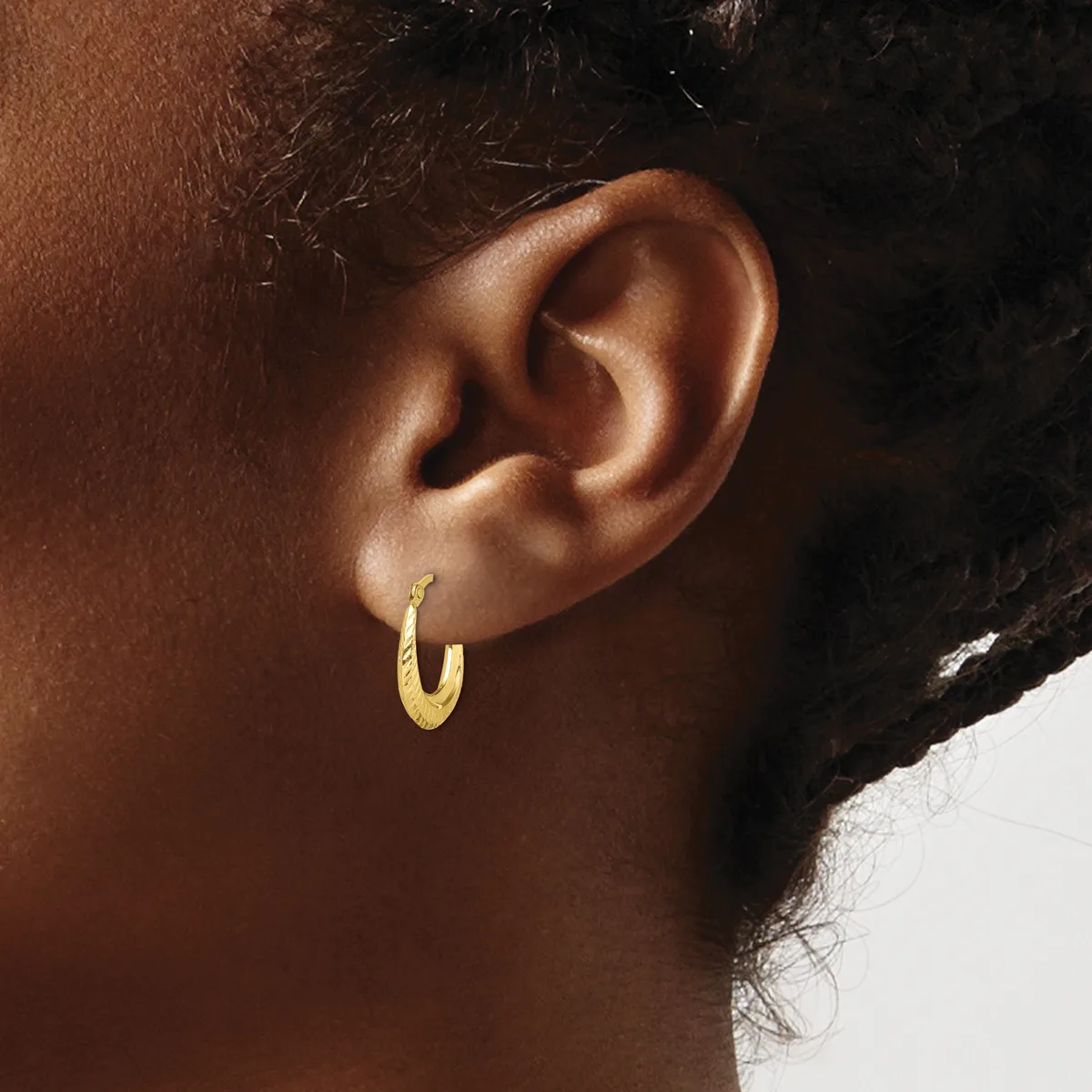 A close-up of a person's ear wearing a small textured gold hoop earring.