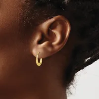A close-up of a person's ear wearing a small textured gold hoop earring.