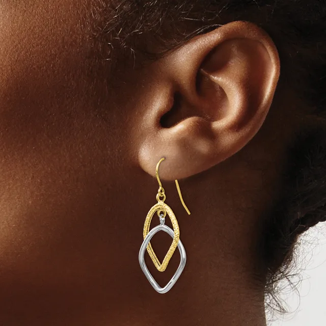A woman wears gold and silver nested diamond-shaped drop earrings with thin wire ear hooks.