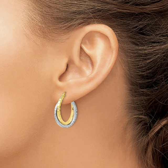 A person wearing two-tone hoop earrings with a textured gold inner surface and polished silver outer surface, shown from the side view against their ear.