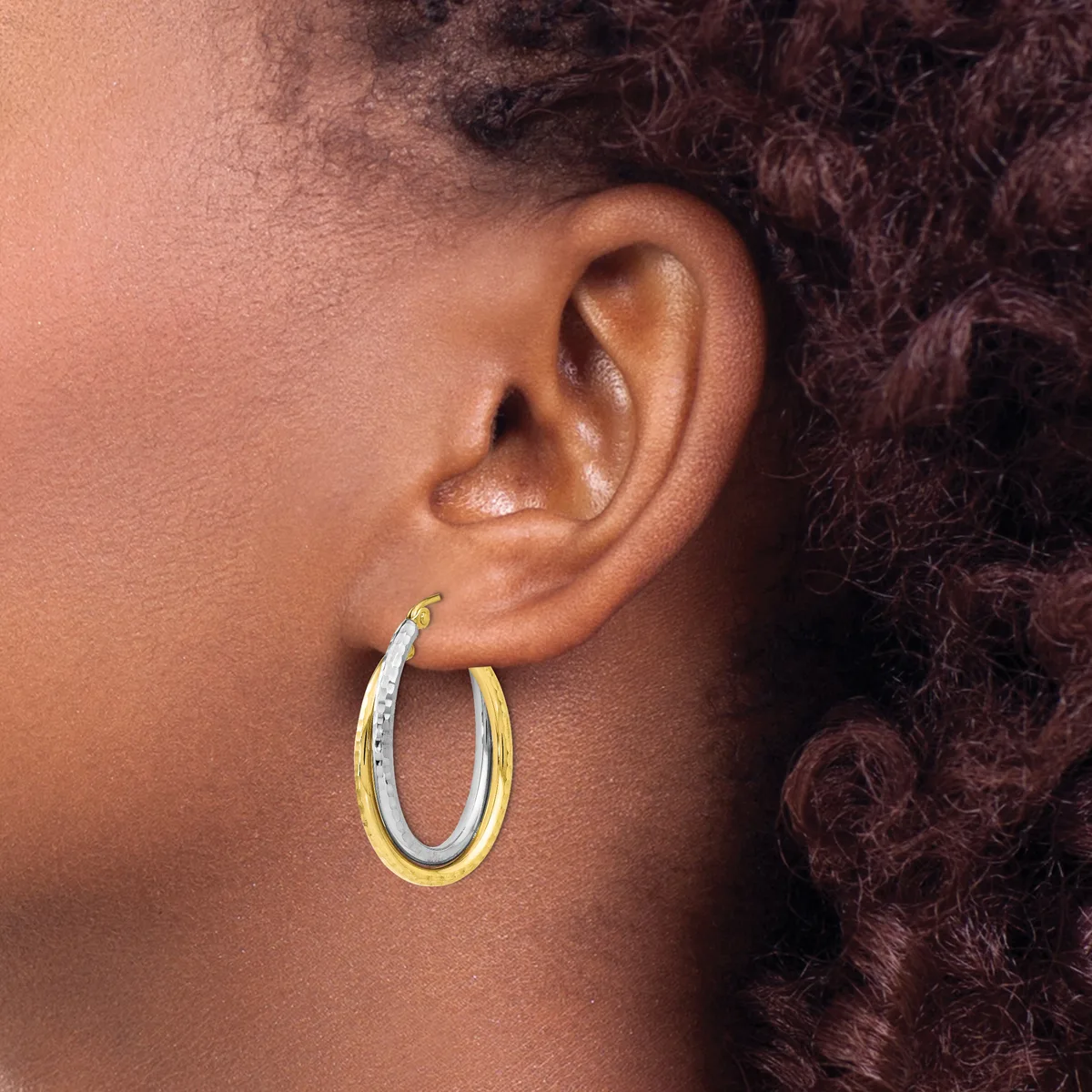 A person wearing two-tone gold and white hoop earrings, shown from the side view with curly dark hair visible.