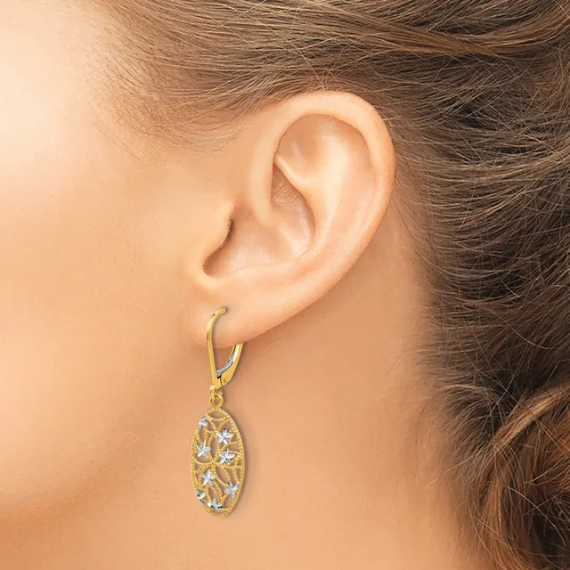A woman wearing a gold-toned lever-back earring with an oval pendant featuring an open filigree design set with clear stones.