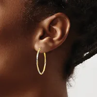 A person wearing a pair of gold hoop earrings with a textured surface, shown from the side view of their ear and neck.