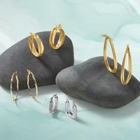 Five pairs of hoop earrings displayed on dark gray stones against a light blue background: three gold-toned pairs in various sizes and textures, and two silver-toned pairs with textured surfaces.