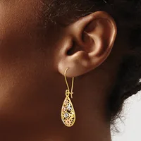 A woman wearing a gold teardrop-shaped filigree earring with an open lattice pattern suspended from a curved wire hook.