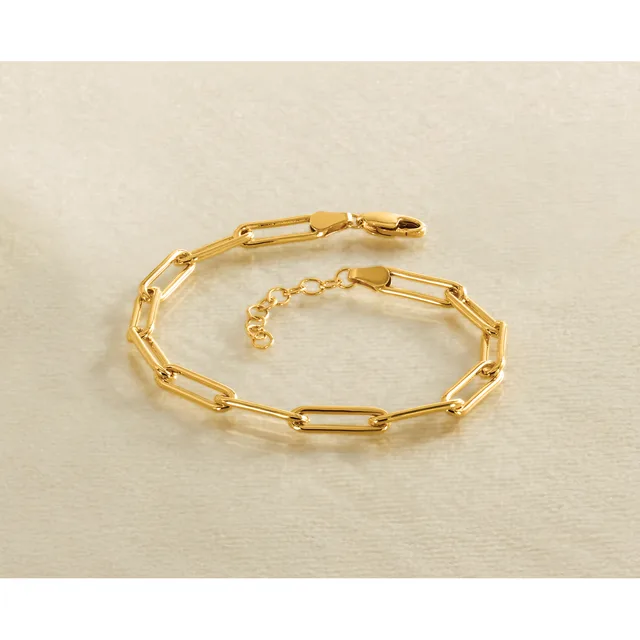 A gold-colored chain bracelet with rectangular paperclip-style links and a lobster claw clasp, displayed on a beige surface.