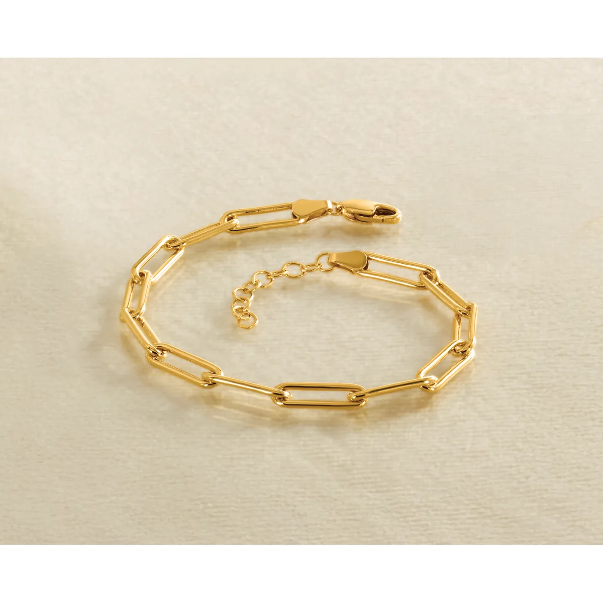 A gold-colored chain bracelet with rectangular paperclip-style links and a lobster claw clasp, displayed on a beige surface.