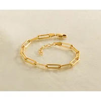 A gold-colored chain bracelet with rectangular paperclip-style links and a lobster claw clasp, displayed on a beige surface.