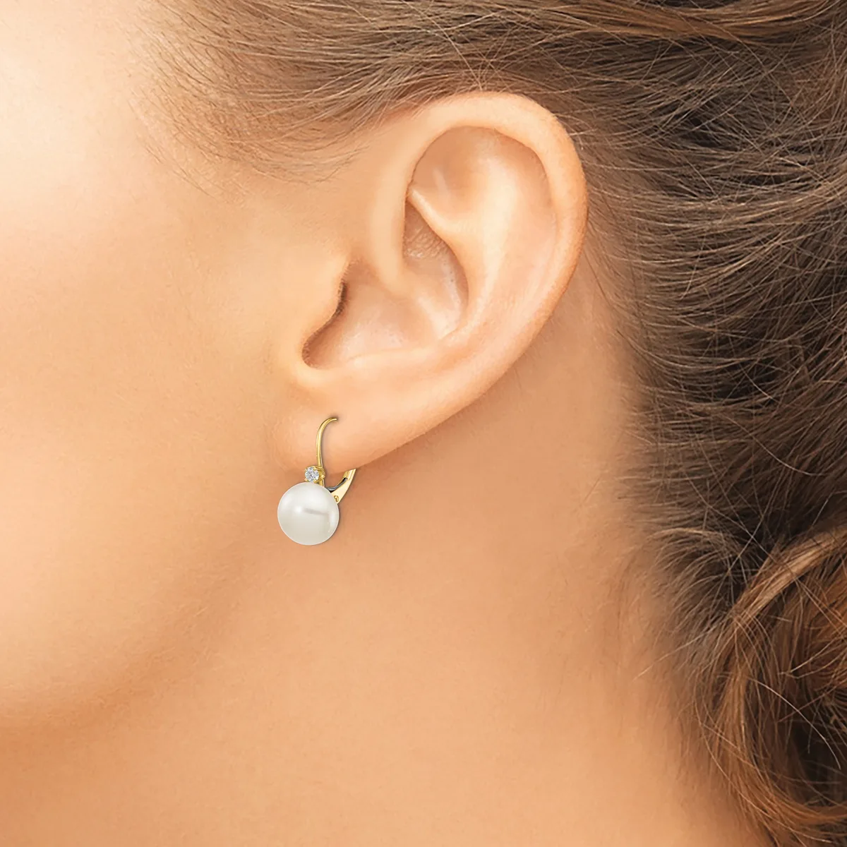 A woman wearing a white pearl drop earring with a curved silver hook, shown from the side profile of her ear and neck.