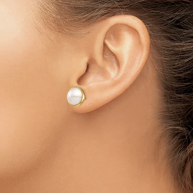 A person wearing a small round pearl stud earring with a gold-toned metal setting in their earlobe.