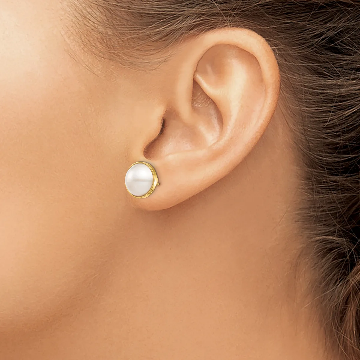 A person wearing a small round pearl stud earring with a gold-toned metal setting in their earlobe.