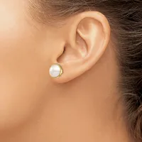 A person wearing a small round pearl stud earring with a gold-toned metal setting in their earlobe.