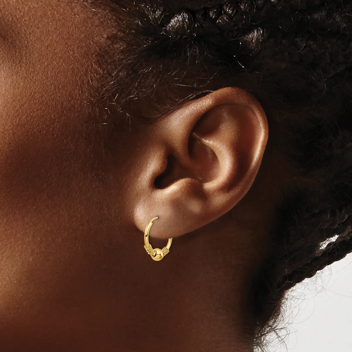 Close-up side view of a person's ear wearing a small gold hoop earring with a textured surface.