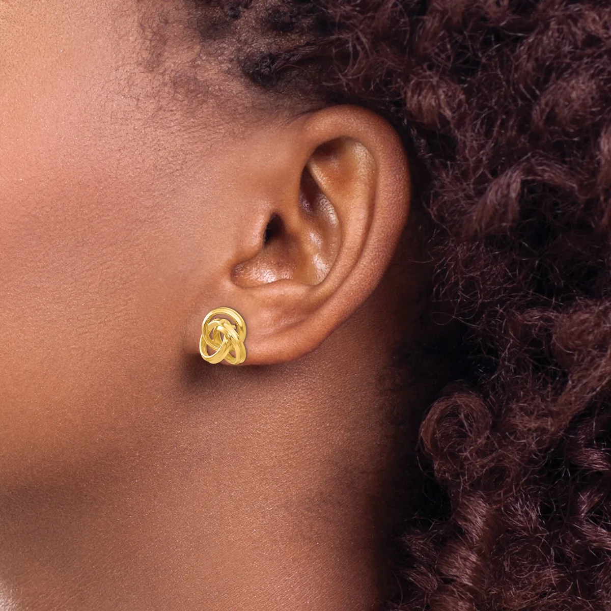 A person wearing a gold-toned chunky curved hoop earring in their earlobe, shown in profile against their shoulder.