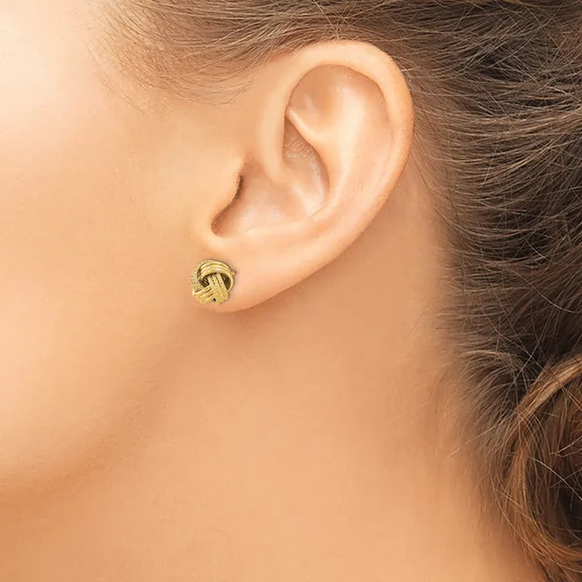 A woman wearing a small gold knotted stud earring in her earlobe, shown from the side view of her ear and neck.
