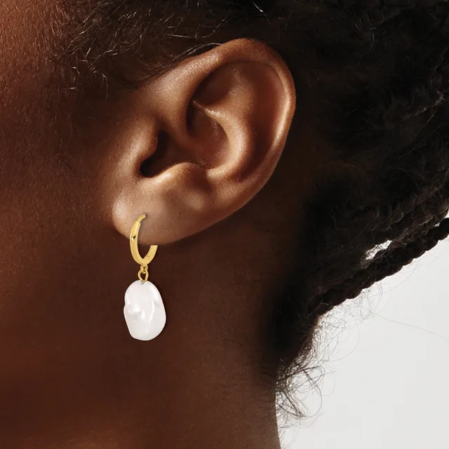 A person wearing a gold hoop earring with a white oval stone pendant hanging from it.