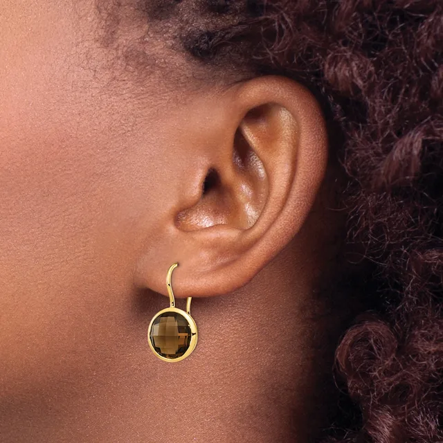 A gold-toned circular drop earring with a checkered brown gemstone center hangs from a pierced earlobe.