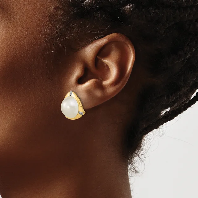 A person wearing a teardrop-shaped earring with a white stone center and gold-toned metal band, shown from the side profile of their ear and neck.