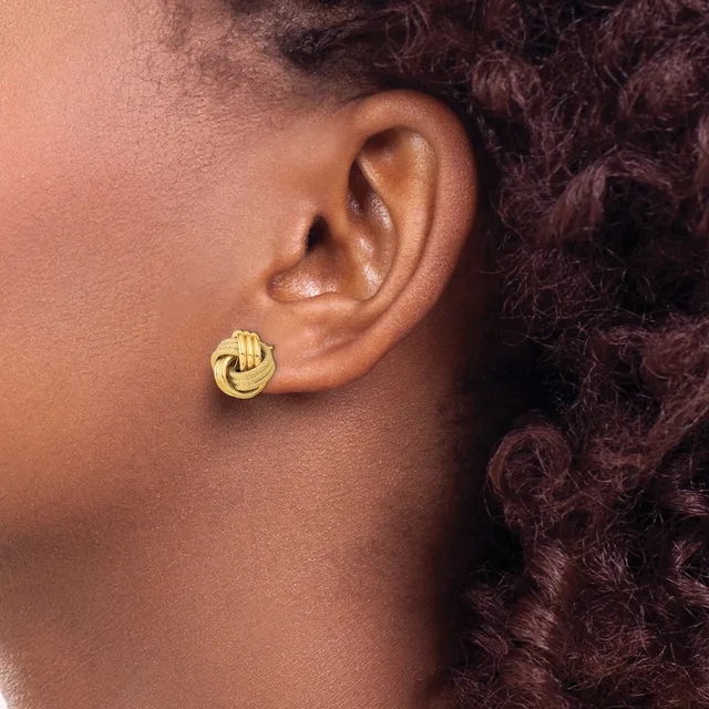 A person wearing a gold-toned twisted knot stud earring in their earlobe, shown in profile against their neck and shoulder.
