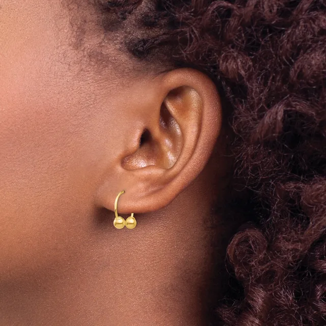 A person wearing gold hoop earrings with small spherical charms, shown from the side profile of their ear and neck.