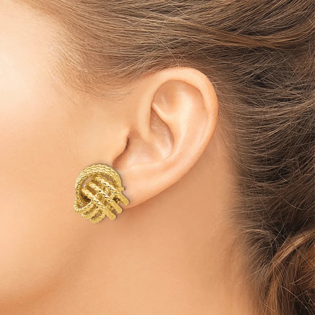 A gold textured clip-on earring with a chunky, organic knot design worn on a person's ear.