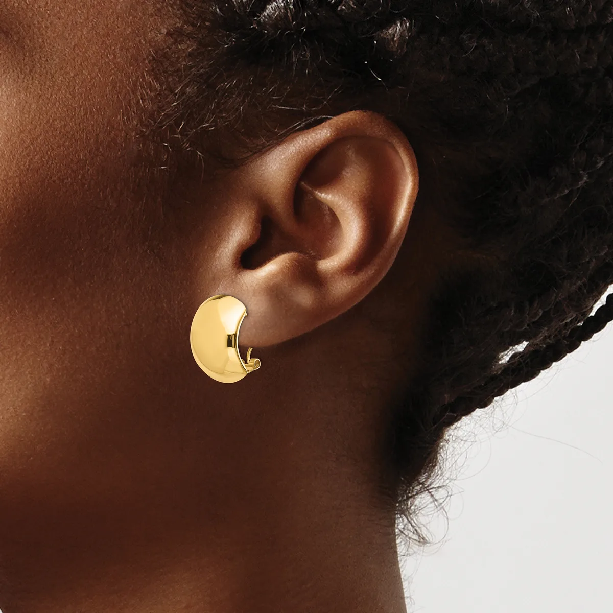 A person wearing a gold-colored curved chunky hoop earring on their earlobe, shown in profile against a neutral background.