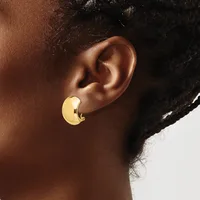 A person wearing a gold-colored curved chunky hoop earring on their earlobe, shown in profile against a neutral background.