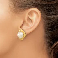 A woman wearing a gold-toned stud earring with a white pearl centered in a textured square setting.