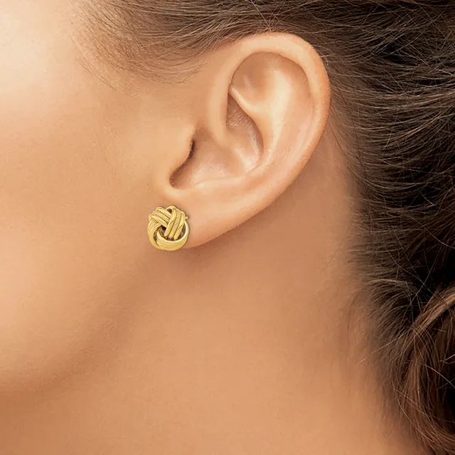 A woman wearing a gold knot stud earring in her earlobe, shown in profile against her bare shoulder and neck.