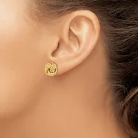 A woman wearing a gold knot stud earring in her earlobe, shown in profile against her bare shoulder and neck.
