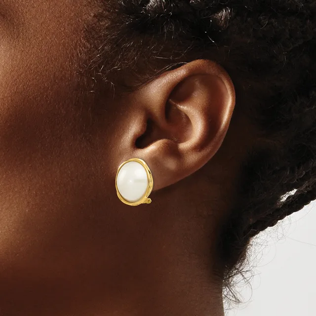 A gold-toned oval earring with a white stone or pearl center on a person's ear, shown in profile against a neutral background.