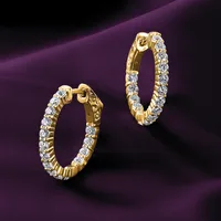 Two gold hoop earrings set with round diamonds arranged in a line, displayed against a purple fabric background.