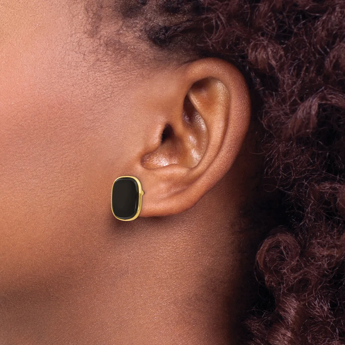 A person wearing a gold-rimmed oval earring with a black center stone in their pierced earlobe, shown in profile.