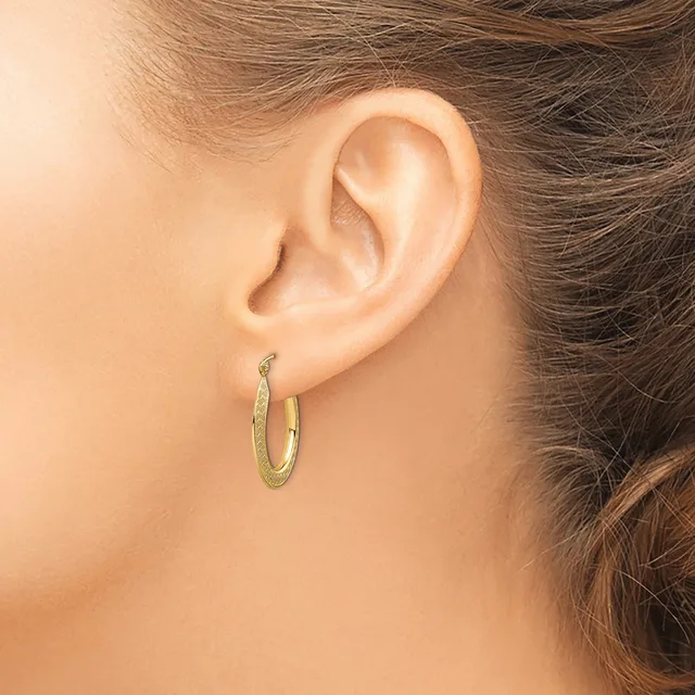 A person wearing small gold hoop earrings with a textured finish, shown from the side profile of their ear and neck.