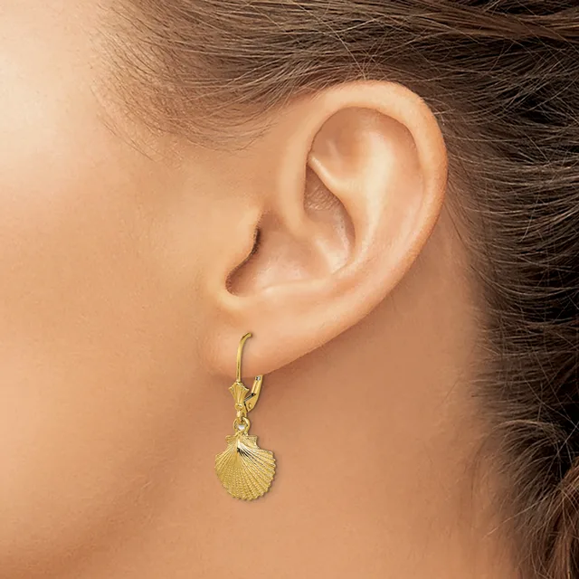 A person wearing a gold shell-shaped dangle earring on a lever-back hook, shown from the side profile of their ear.