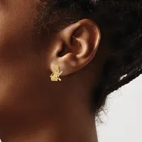 A gold stud earring with a textured rectangular design is worn on the earlobe of a person with deep skin tone and dark hair.