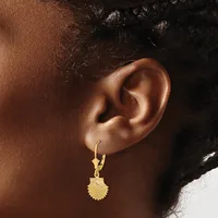 A person wearing a gold scallop shell-shaped pendant earring on a lever-back hook, shown from the side against their ear.