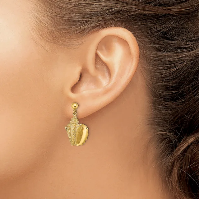 A person wearing a gold-toned shell-shaped dangle earring with textured detailing on the upper portion, shown from the side view of their ear.