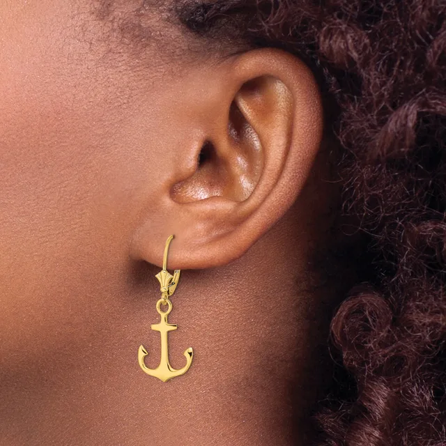 A gold-toned anchor-shaped earring hangs from a lever-back hook on a person's earlobe.
