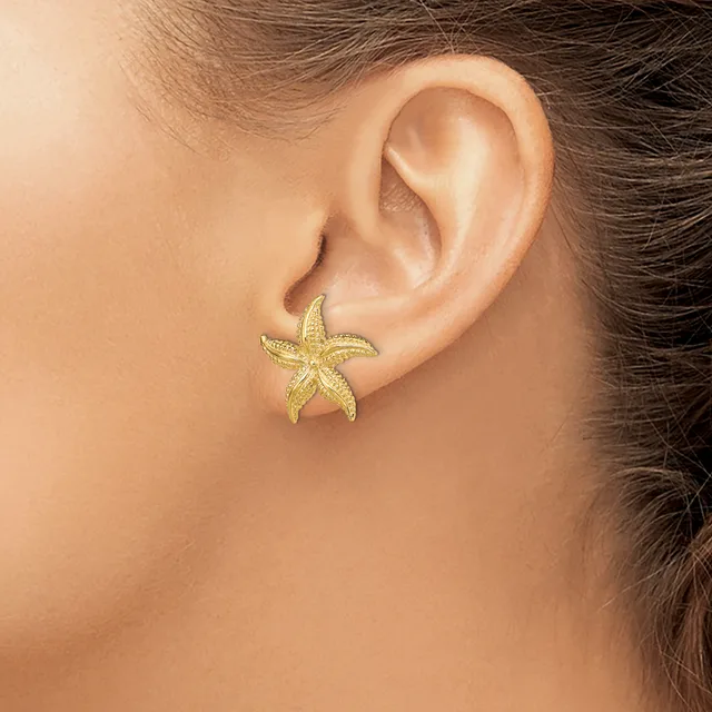 A gold starfish-shaped earring stud is worn on the earlobe of a person shown in profile.