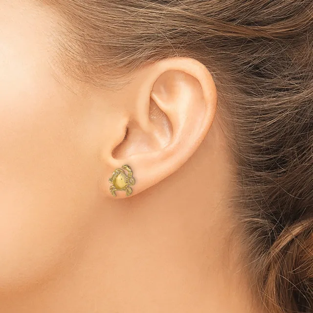 A gold-toned crab-shaped earring with a pale yellow stone center on a wearer's ear lobe.