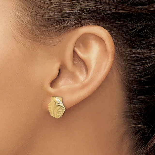 A gold shell-shaped stud earring worn on a person's earlobe, shown in profile view.