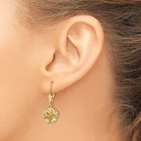 A woman wearing a gold-toned flower-shaped dangle earring with a lever back clasp, shown from the side profile of her ear.