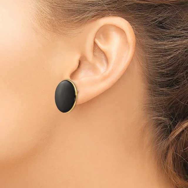 A person wearing a black oval earring with a gold-tone metal bezel, shown from the side view against their ear.