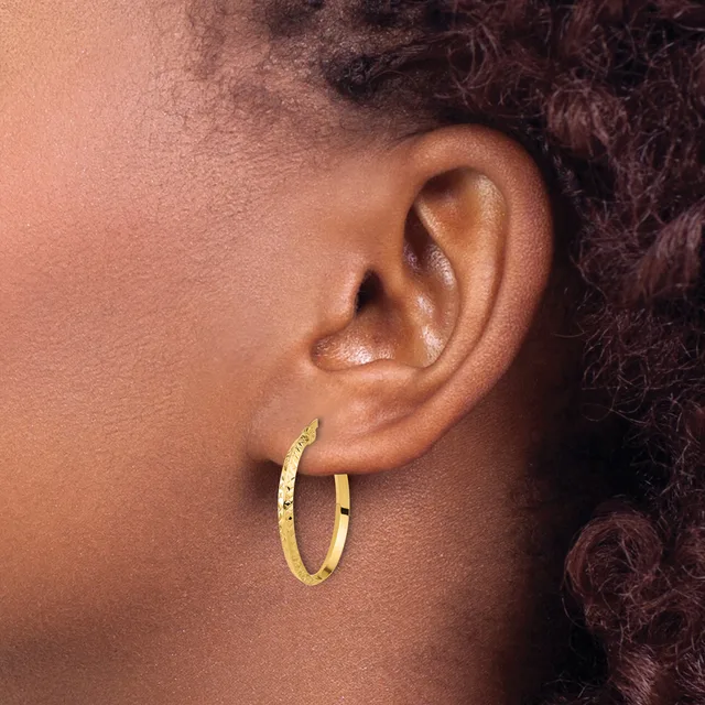 A person wearing gold hoop earrings with a textured finish, shown in profile against a neutral background.