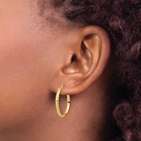 A person wearing gold hoop earrings with a textured finish, shown in profile against a neutral background.
